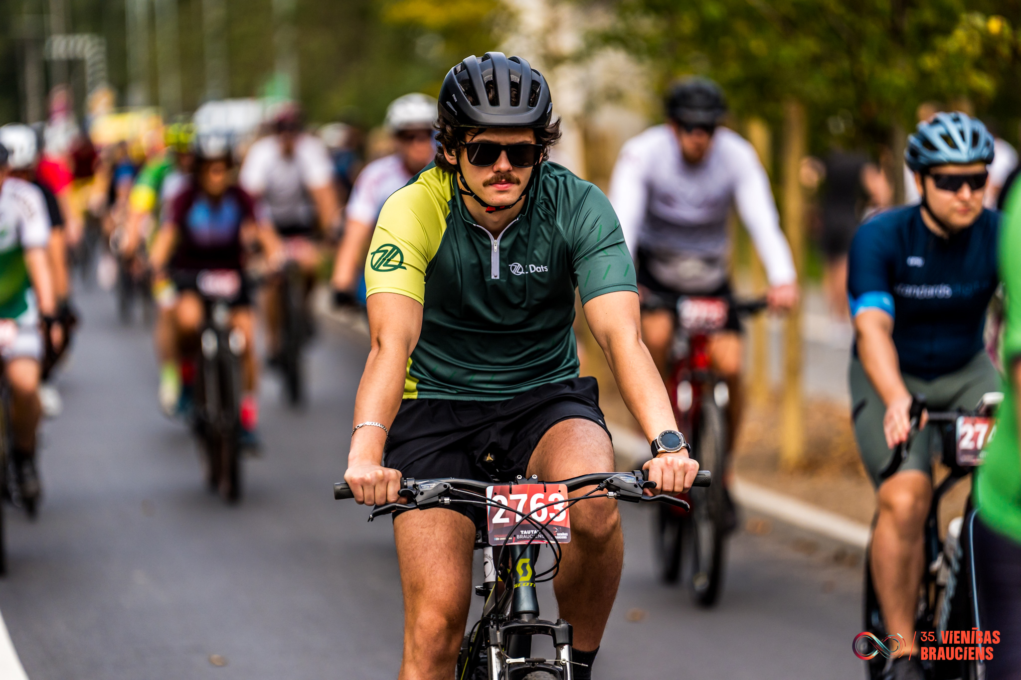 Cyclists participating in a road cycling race event with riders wearing helmets and numbered bibs outdoors