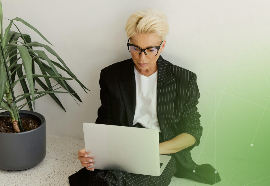 A woman is sitting on the floor next to a flower pot, working on her computer